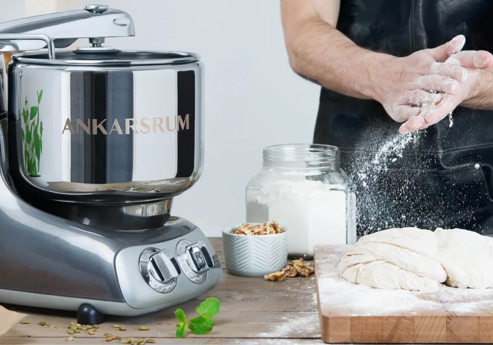 Ankarsrum Maschine neben einer Person mit Mehl in der Hand und einem Brotteig auf dem Tisch
