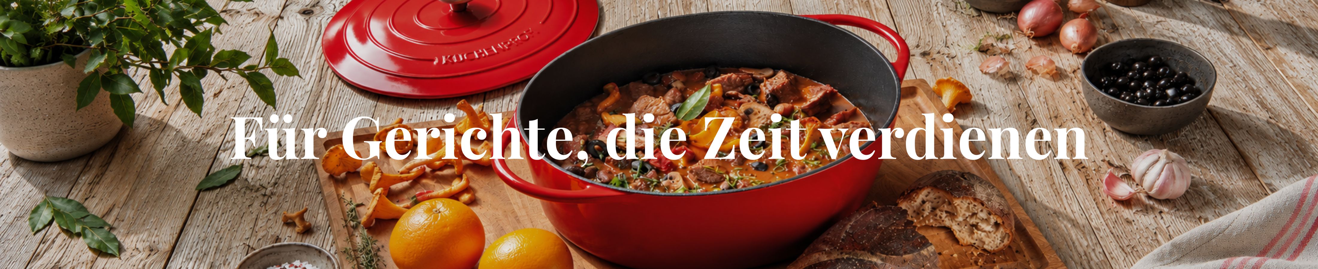 Roter Gusseisenbräter von KÜCHENPROFI mit Schmorgericht auf gedecktem Holztisch