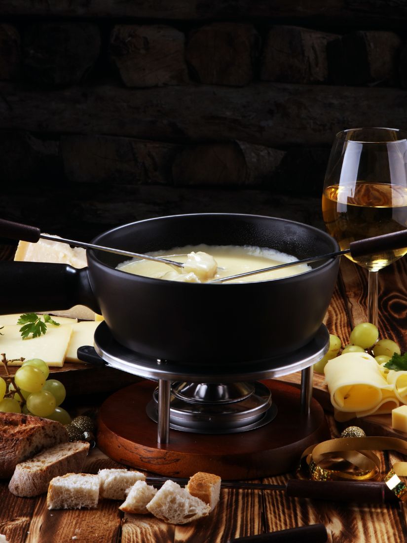 Käsefondue mit Zutaten auf einem gedeckten Tisch Käsefondue mit Zutaten auf einem gedeckten Tisch